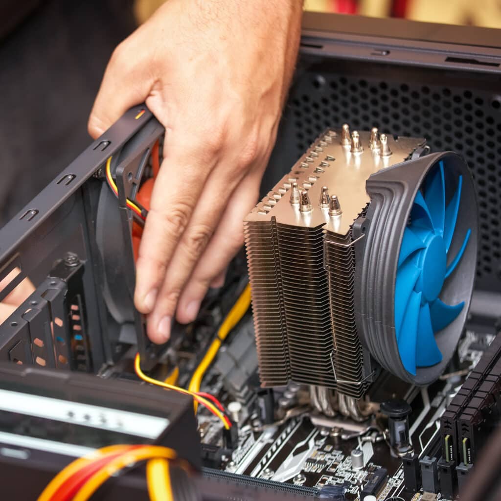 Main installant un ventilateur noir dans un boîtier PC. Un grand refroidisseur CPU avec un ventilateur bleu et une carte mère sont visibles.